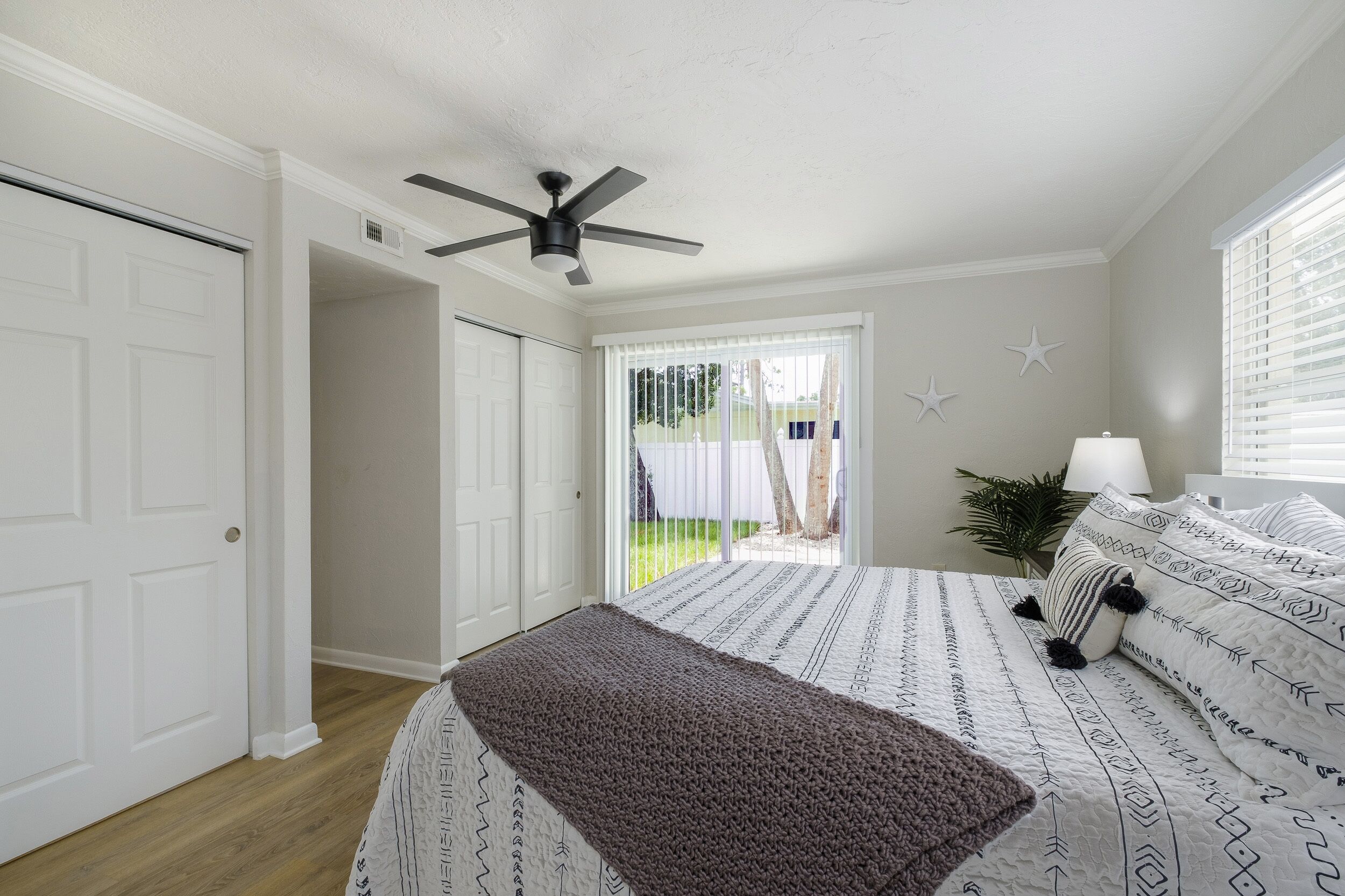 Une chambre à coucher avec un lit, un ventilateur de plafond, une fenêtre avec des stores et une porte.