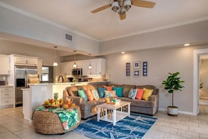A spacious living room with a sofa, coffee table, and a dining area with a kitchen in the background.