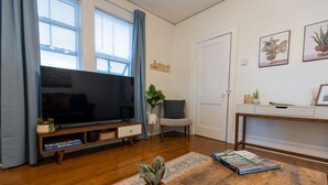 A living room with a flat-screen TV, a sofa, a coffee table, and a bookshelf. - Historic Revival King Bed Midtown Memphis 68 (Memphis)