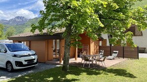 A white car parked in front of a wooden cabin with a patio area, a table, and chairs.