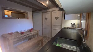 A compact kitchen with a wooden countertop, a sink, and a mirror above it. There are two doors with heart-shaped decorations and a bench in the corner.