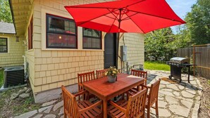 Une petite maison en bois avec un patio, un parasol rouge et un barbecue.