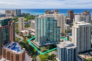 A high-rise building with a rooftop pool, surrounded by other high-rise buildings and a clear view of the ocean.