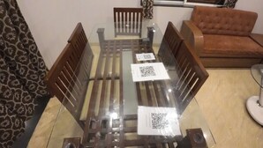A dining area with a glass-top table, wooden chairs, and a brown sofa. - Royal Palace Panchgani (Mahabaleshwar)