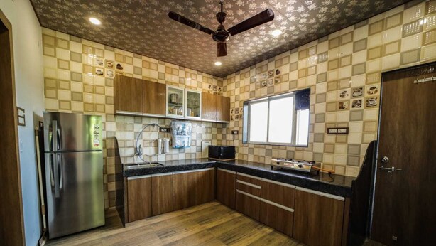 A kitchen with wooden cabinets, a stainless steel refrigerator, a gas stove, and a ceiling fan. - Royal Palace Panchgani (Mahabaleshwar)