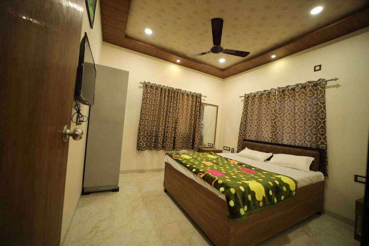 A bedroom with a bed, a ceiling fan, a mirror, and patterned curtains.
