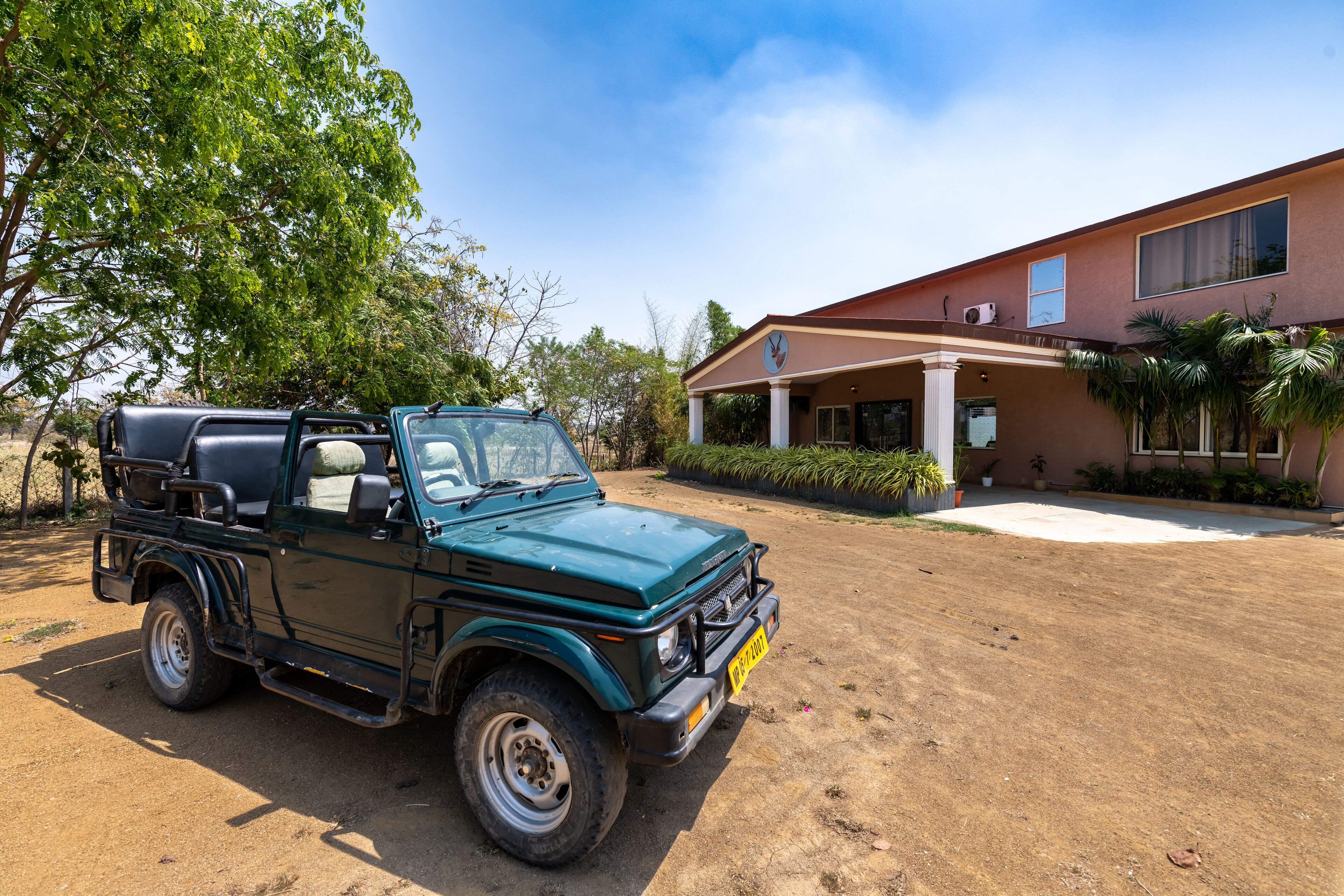 A green off-road vehicle parked in front of a building with a covered entrance and a palm tree.