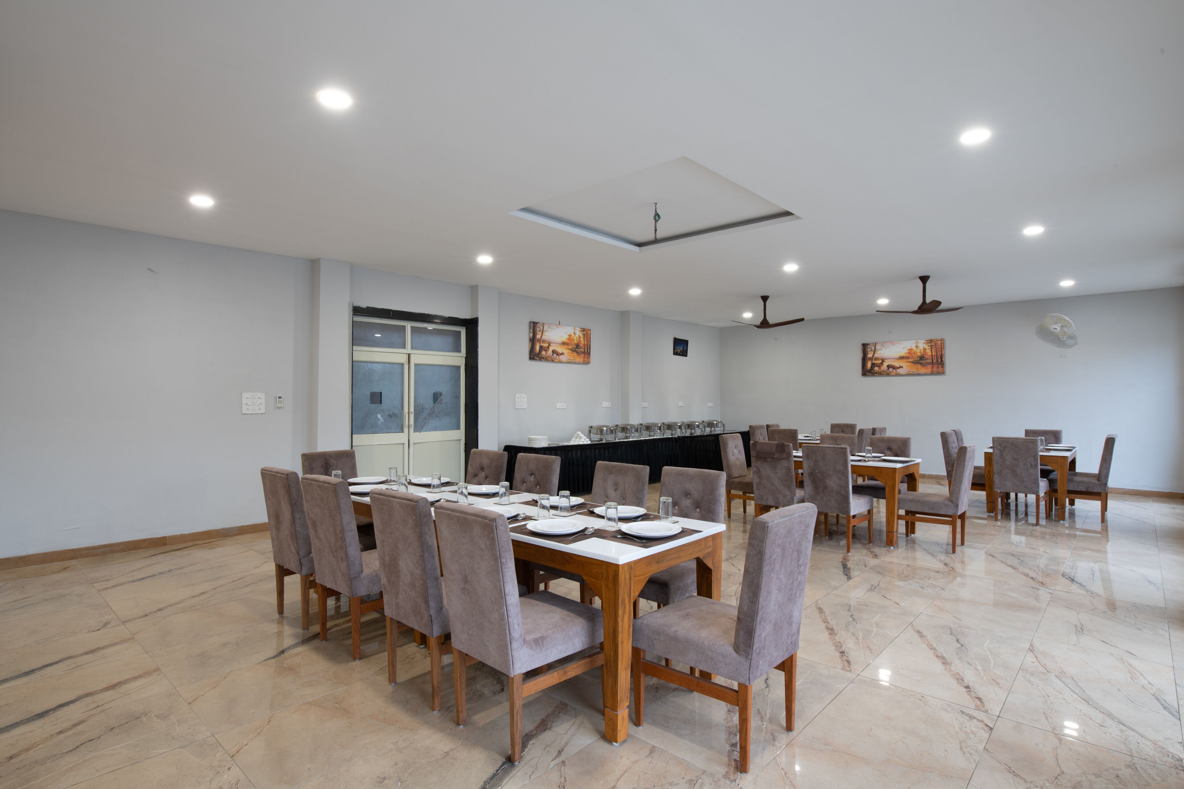 Un comedor amplio con varias mesas y sillas, un ventilador de techo e iluminación empotrada.