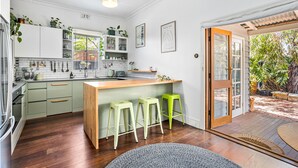 A modern kitchen with white cabinets, a wooden island, and green bar stools. - Saltbush Cottage in fabulous South Fremantle. (South Fremantle)