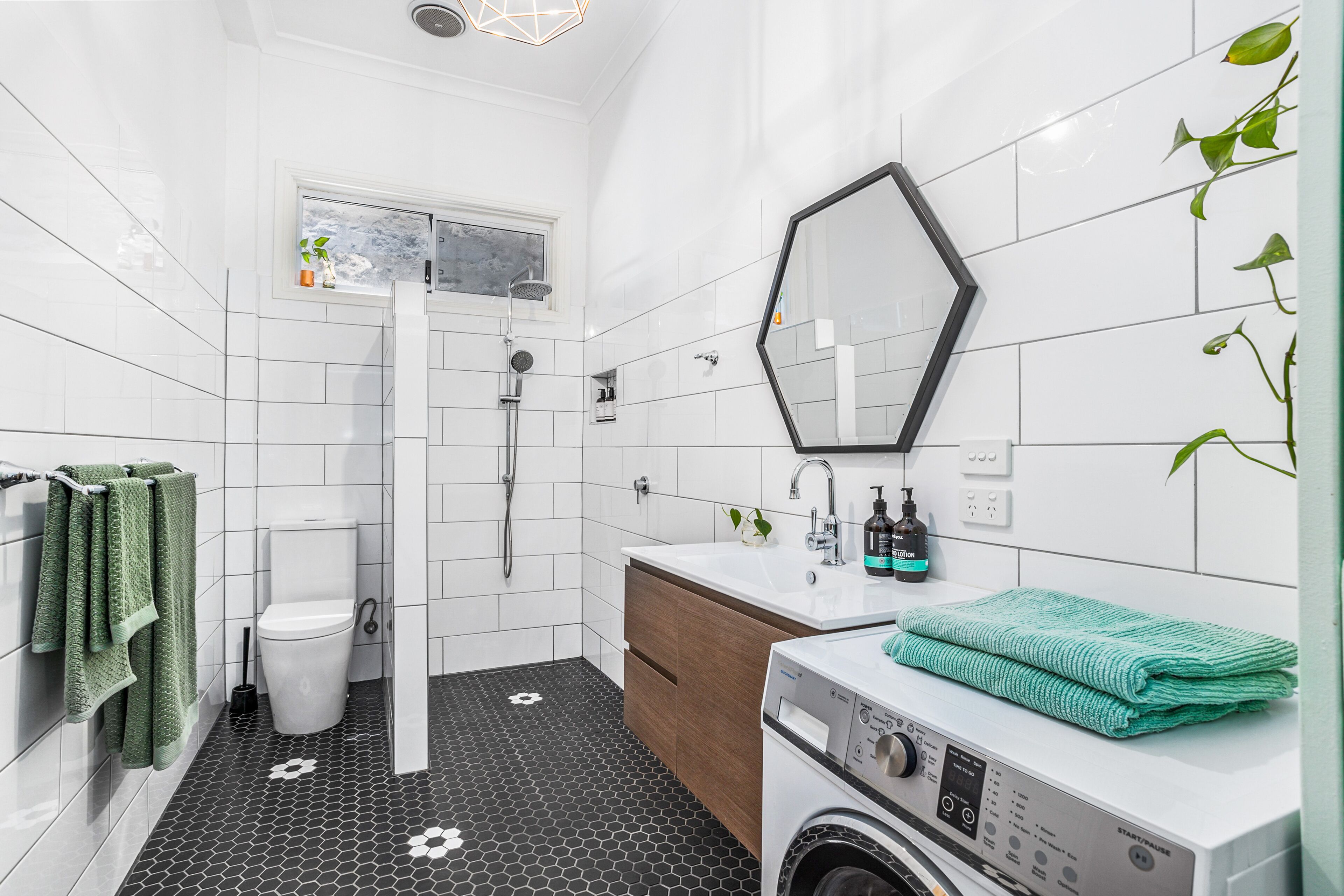 Een moderne badkamer met een wit toilet, een douche, een wastafel met spiegel en een wasmachine.