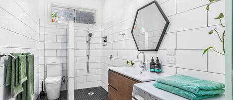 Een moderne badkamer met een wit toilet, een douche, een wastafel met spiegel en een wasmachine.