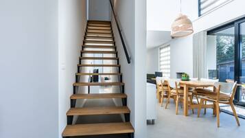 Een moderne trap met houten treden en een zwarte leuning, die leidt naar een eetgedeelte met een tafel en stoelen.
