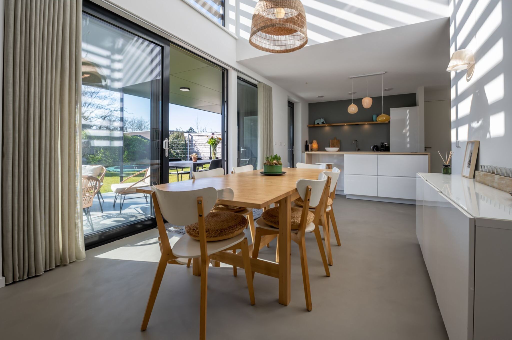 Een moderne keuken met witte kasten, een houten eettafel en uitzicht naar buiten.
