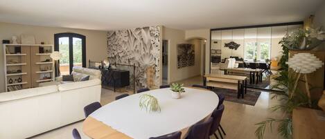 A modern living room with a large round table, purple chairs, a white sofa, and a bookshelf.