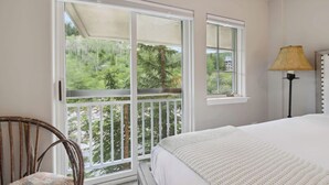 A bedroom with a large bed, a chair, and a view of a balcony with trees. - Saint James Place 333A (Avon)