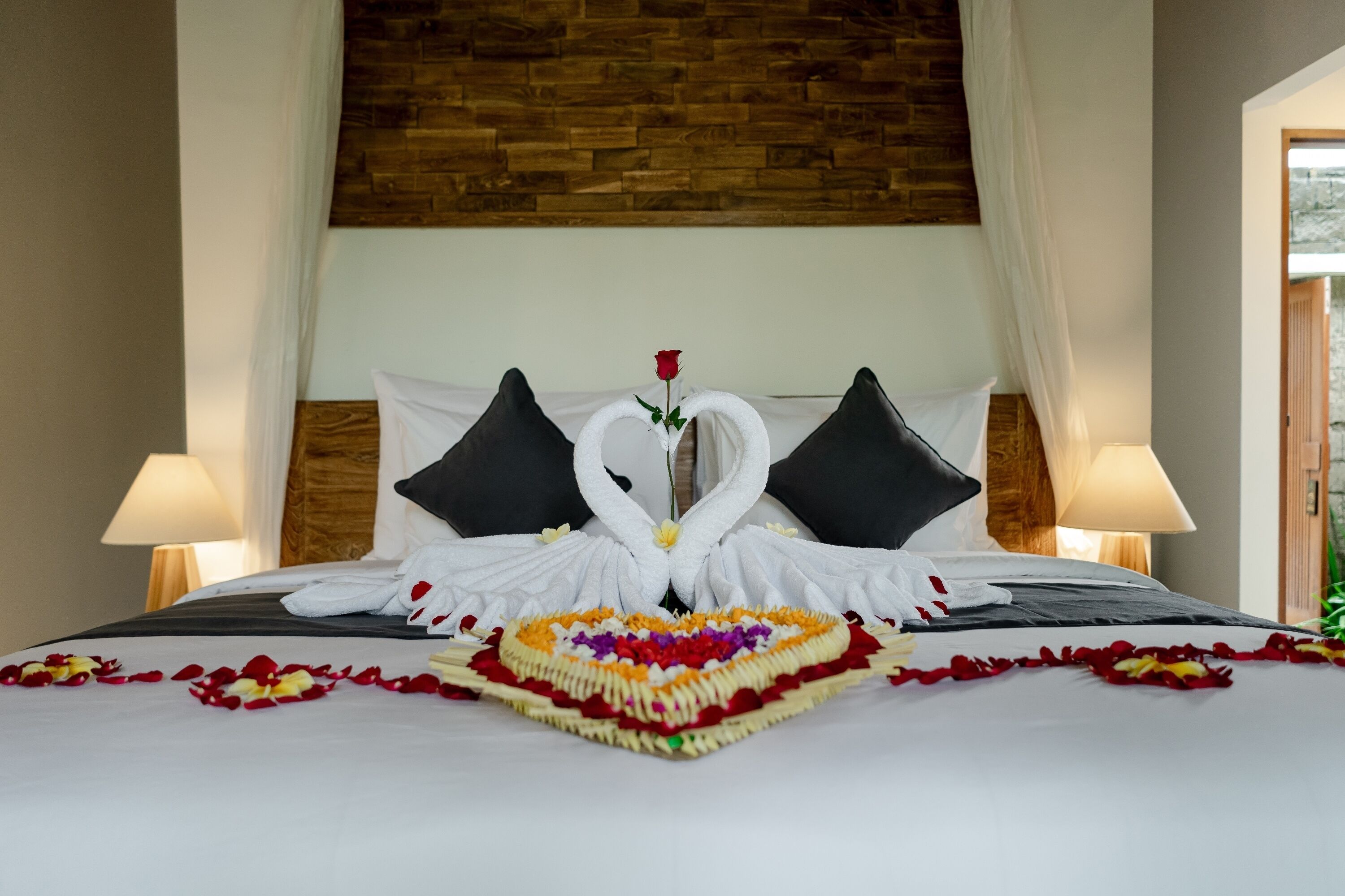 A bed with a heart-shaped flower arrangement and two swan-shaped towels.