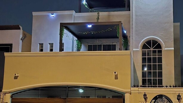 Un edificio de dos pisos con un amplio portón de garaje, un balcón con plantas y un arco decorativo.