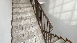 Una escalera con baldosas de mármol y barandilla de madera que conduce a una habitación con ventilador de techo y una puerta al fondo.