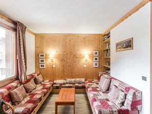 A cozy room with wooden walls, a sofa set, a wooden coffee table, and wall-mounted lamps.