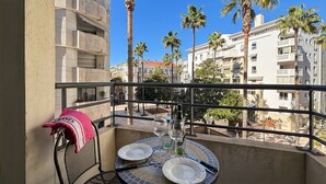 A balcony with a table set for two, overlooking a residential area with palm trees and multi-story buildings. - Modern 2 Bd Next To Rue D'antibes (Cannes)