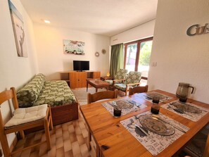 A cozy room with a sofa, a TV, a dining table set for four, and a window with curtains.