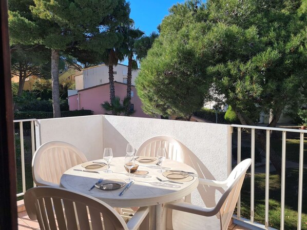 An outdoor dining area with a round table set for four, surrounded by white chairs.