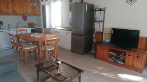 Una cocina compacta con armarios de madera, una mesa de comedor con sillas, un refrigerador, un televisor sobre un mueble de madera y una mesa de centro de vidrio.