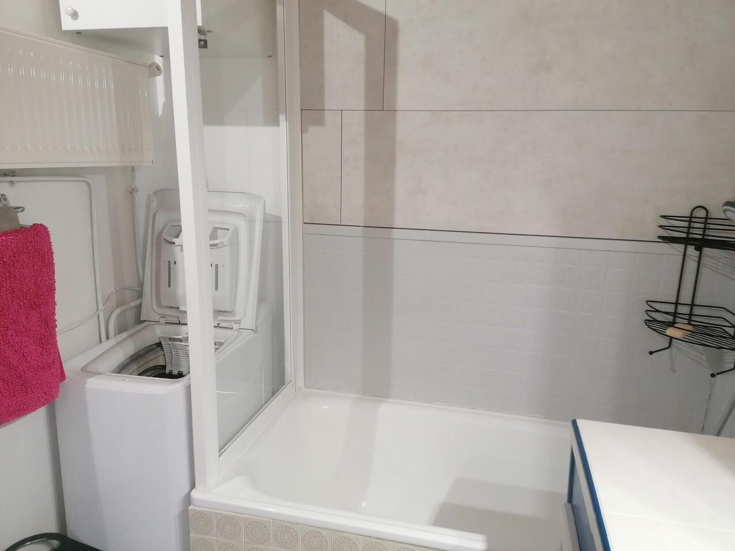 Une salle de bain avec une baignoire blanche, un espace douche et un porte-serviettes sur lequel est posée une serviette rose.