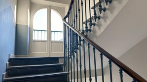 Un escalier aux marches en bois foncé et aux balustrades noires, menant à une porte blanche dotée d’un panneau de verre.