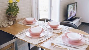A dining table set with pink plates and clear glasses, a wicker basket with flowers, and a television in the background.