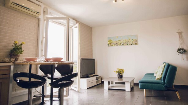 A modern living room with a TV, a dining area with chairs, a sofa, and a painting on the wall.