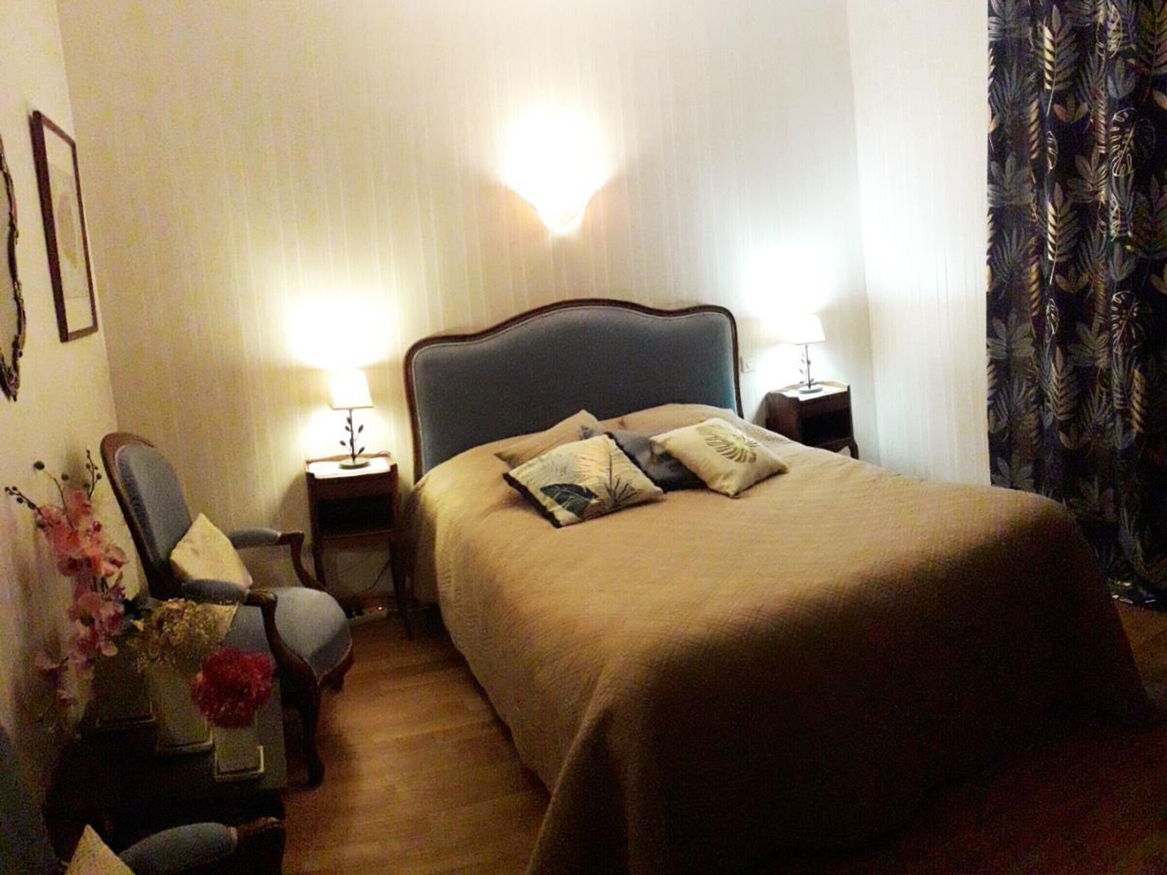 Une chambre d’hôtel avec un grand lit, deux tables de chevet avec des lampes, une chaise et une petite table sur laquelle est posé un vase de fleurs.