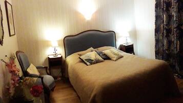 Une chambre d’hôtel avec un grand lit, deux tables de chevet avec des lampes, une chaise et une petite table sur laquelle est posé un vase de fleurs.