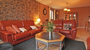 A living room with a red leather sofa, a glass coffee table, and a patterned wallpaper. - Family country house with garden, near Haras du Pin, peaceful and pleasant (Le Merlerault)