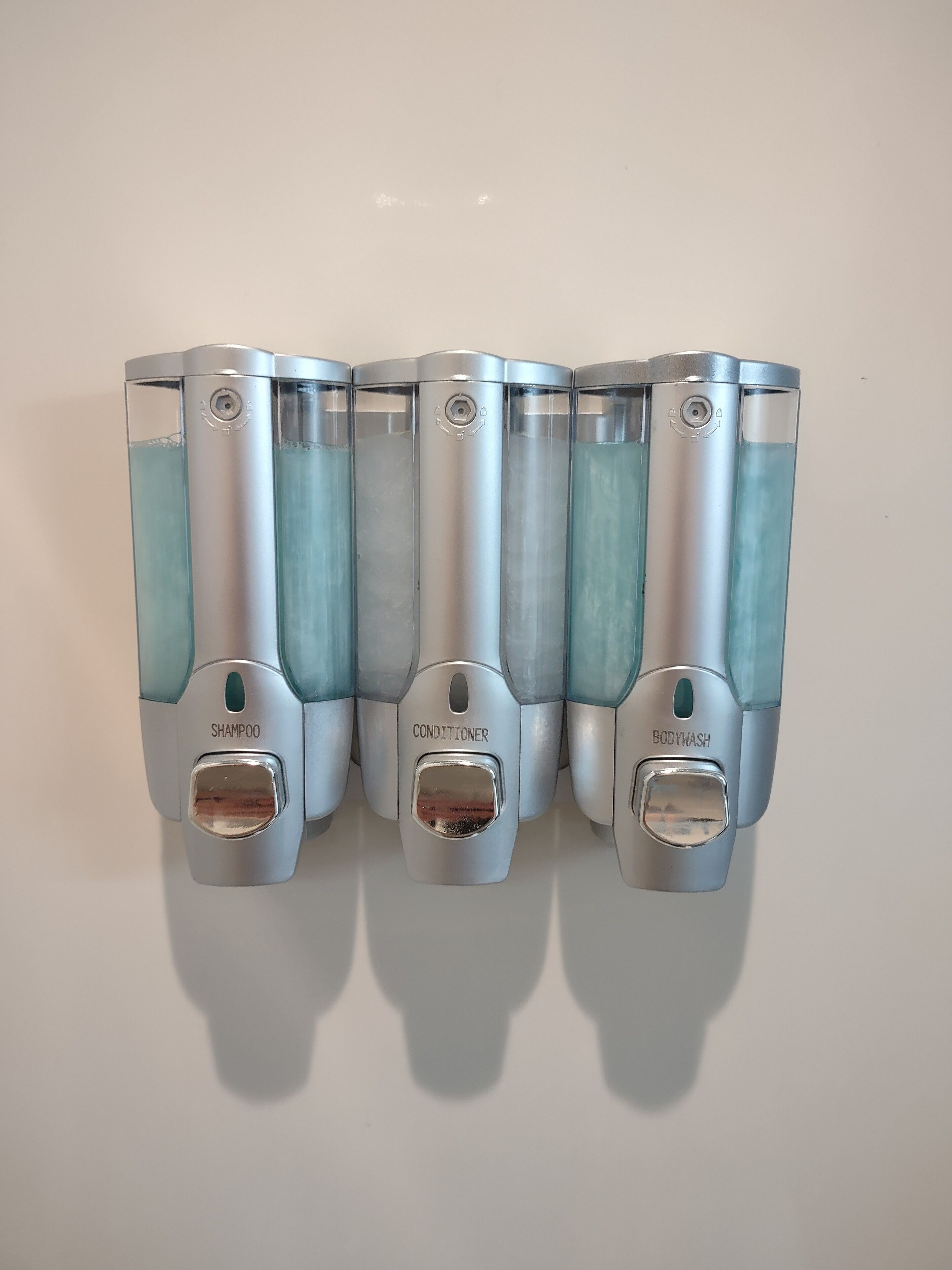 A row of three dispensers labeled shampoo, conditioner, and body wash.