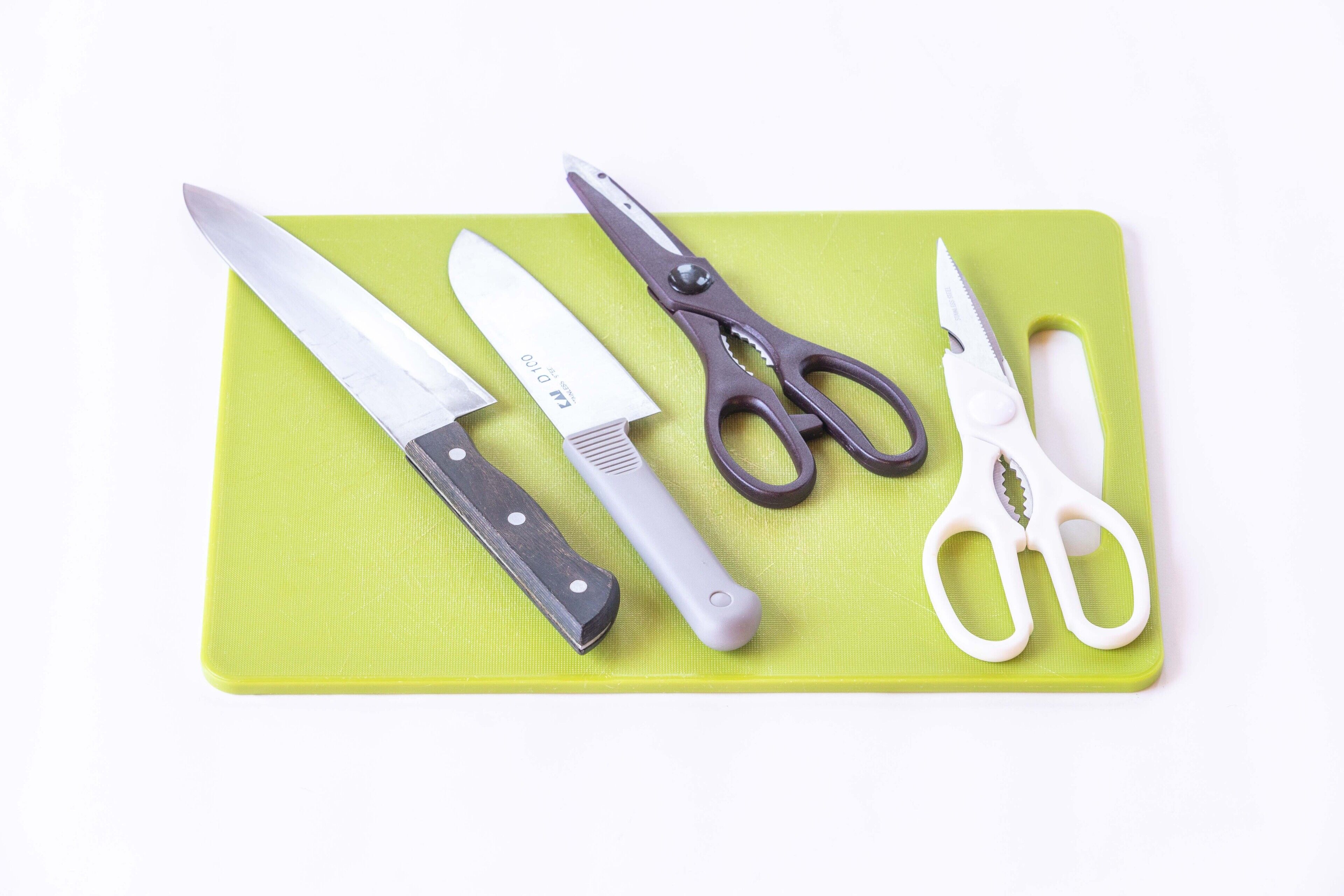 A green cutting board with a knife, a pair of scissors, and a pair of shears.