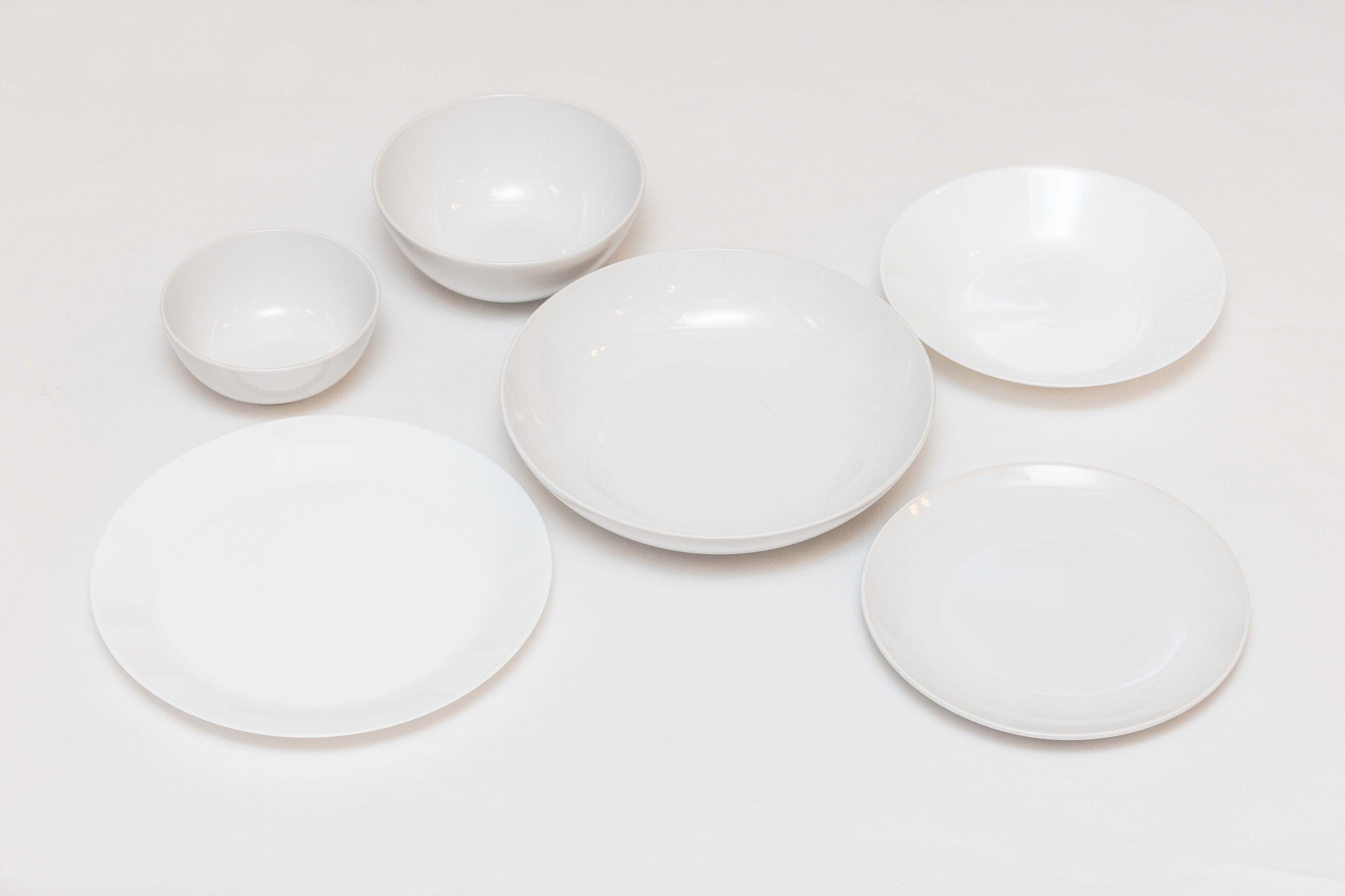 Six white plates of varying sizes arranged on a plain surface.