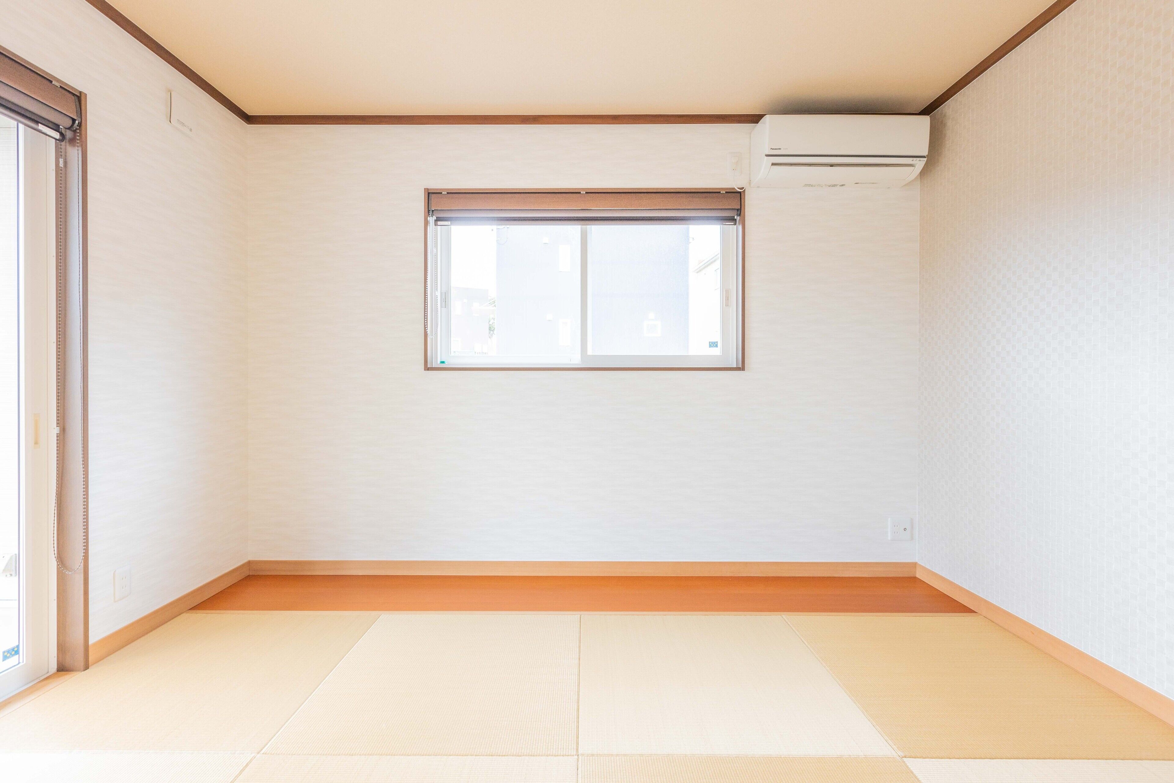 A room with tatami flooring, a sliding door, a window with a blind, and an air conditioning unit on the wall.