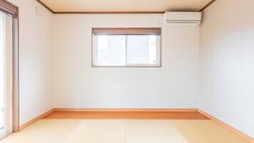 A room with tatami flooring, a sliding door, a window with a blind, and an air conditioning unit on the wall.