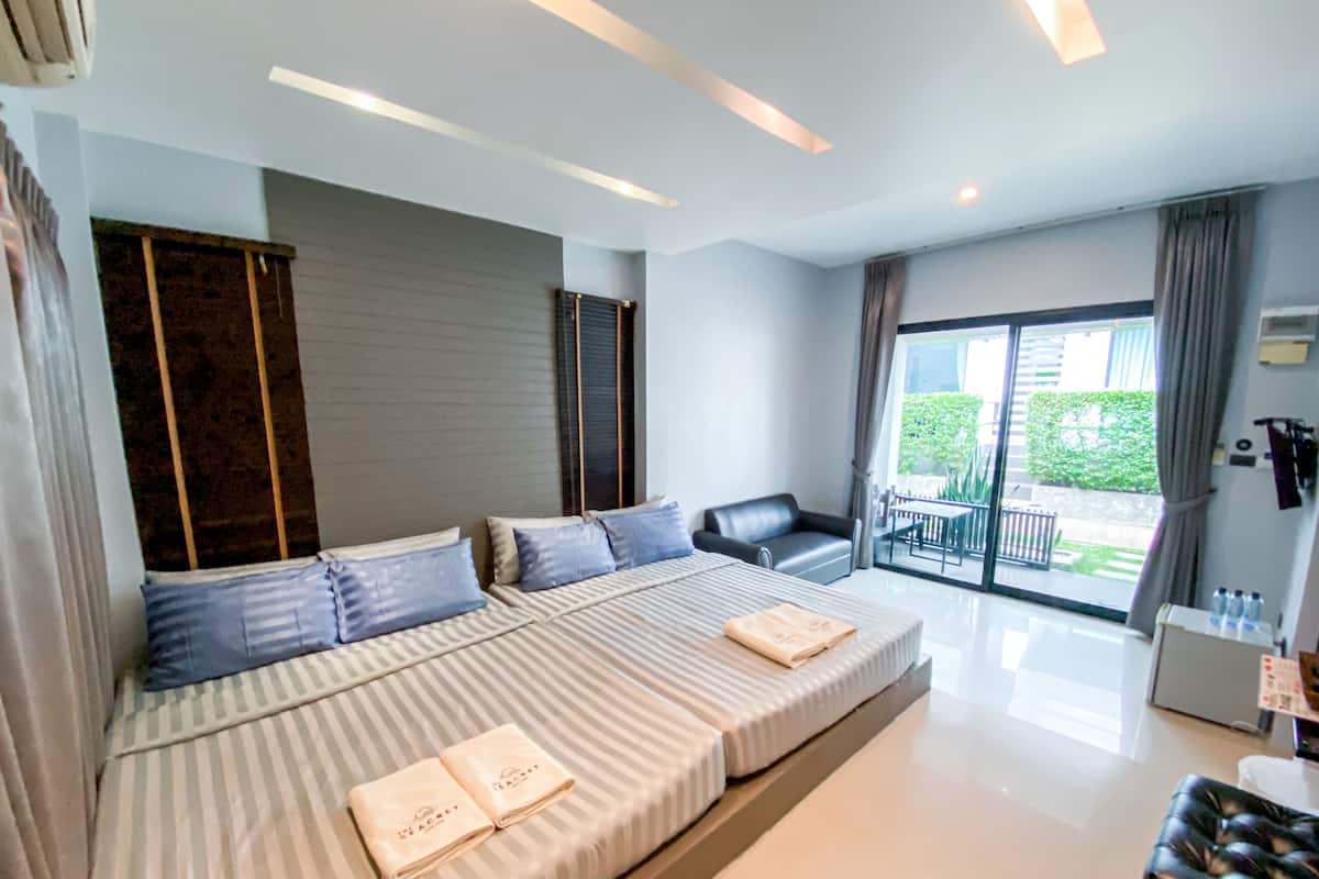 A modern hotel room with a large bed, a sofa, and a balcony with a view of greenery.
