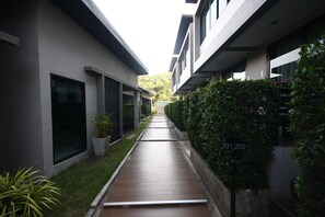 A modern building with a narrow pathway leading to a gate, surrounded by greenery and a clear sky. - The Seacret Kohlarn (Koh Lan)