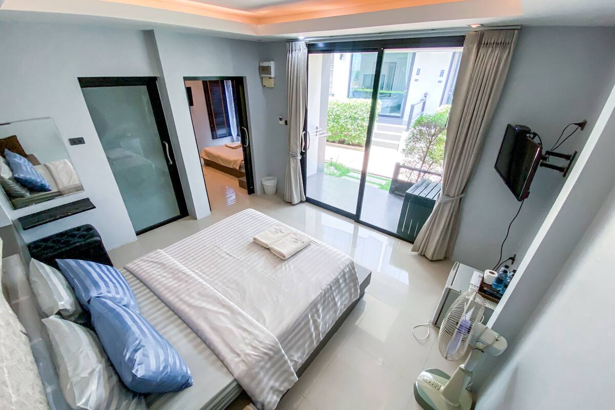 A modern hotel room with a large bed, a sitting area, a balcony with a view, and a TV mounted on the wall.