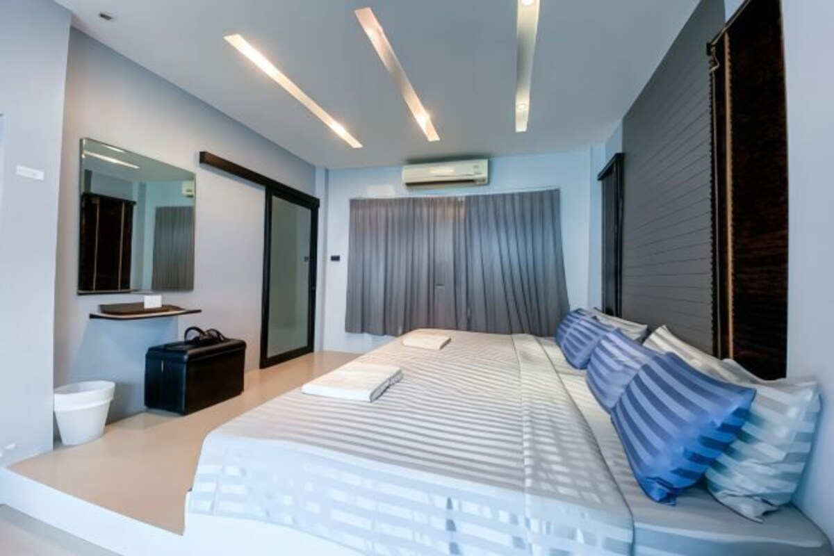 A modern bedroom with a large bed, a bedside table, a mirror, and a window with curtains.