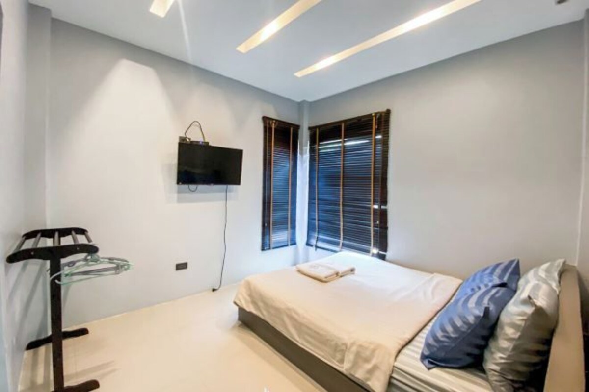 A modern bedroom with a bed, a TV mounted on the wall, and a window with blinds.