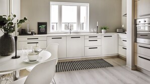 A modern kitchen with white cabinetry, a large window, and a dining area with a table and chairs. - Staysville – City Center (Stavanger)