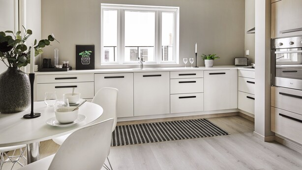 A modern kitchen with white cabinetry, a large window, and a dining area with a table and chairs. - Staysville – City Center (Stavanger)