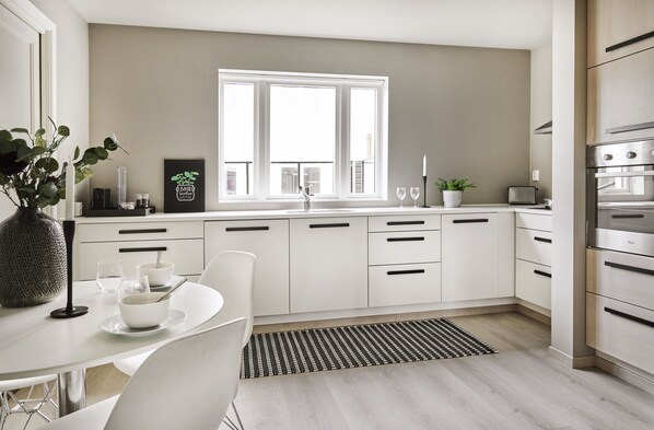 Una cucina moderna con mobili bianchi, un'ampia finestra e un'area pranzo con tavolo e sedie.