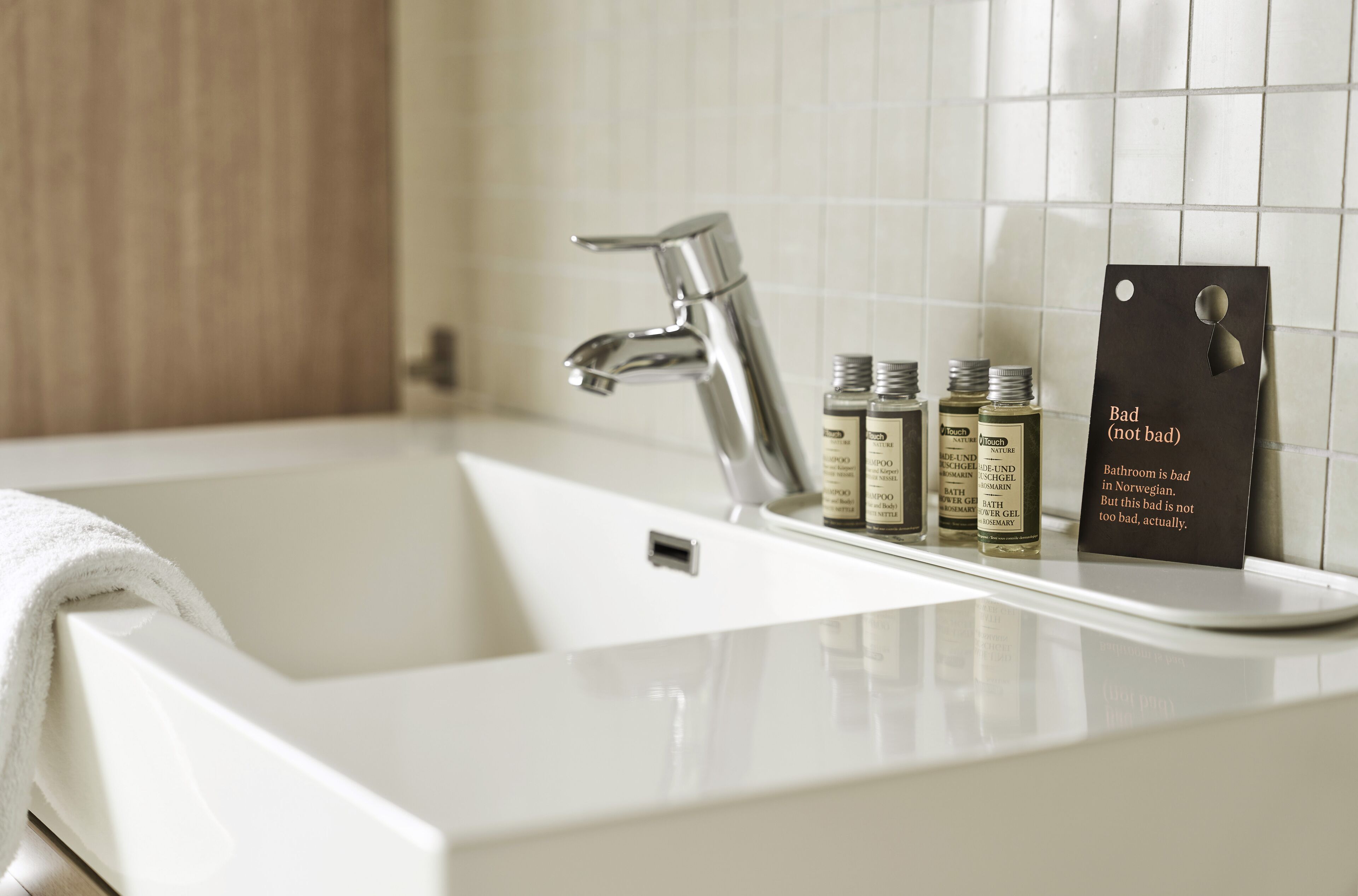 A bathroom with a white sink, a modern faucet, and toiletries. There's a sign that reads "Bad (not bad)".