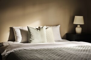 Una cama bien hecha con un edredón acolchado y varias almohadas, una lámpara de noche y una mesita de noche oscura.