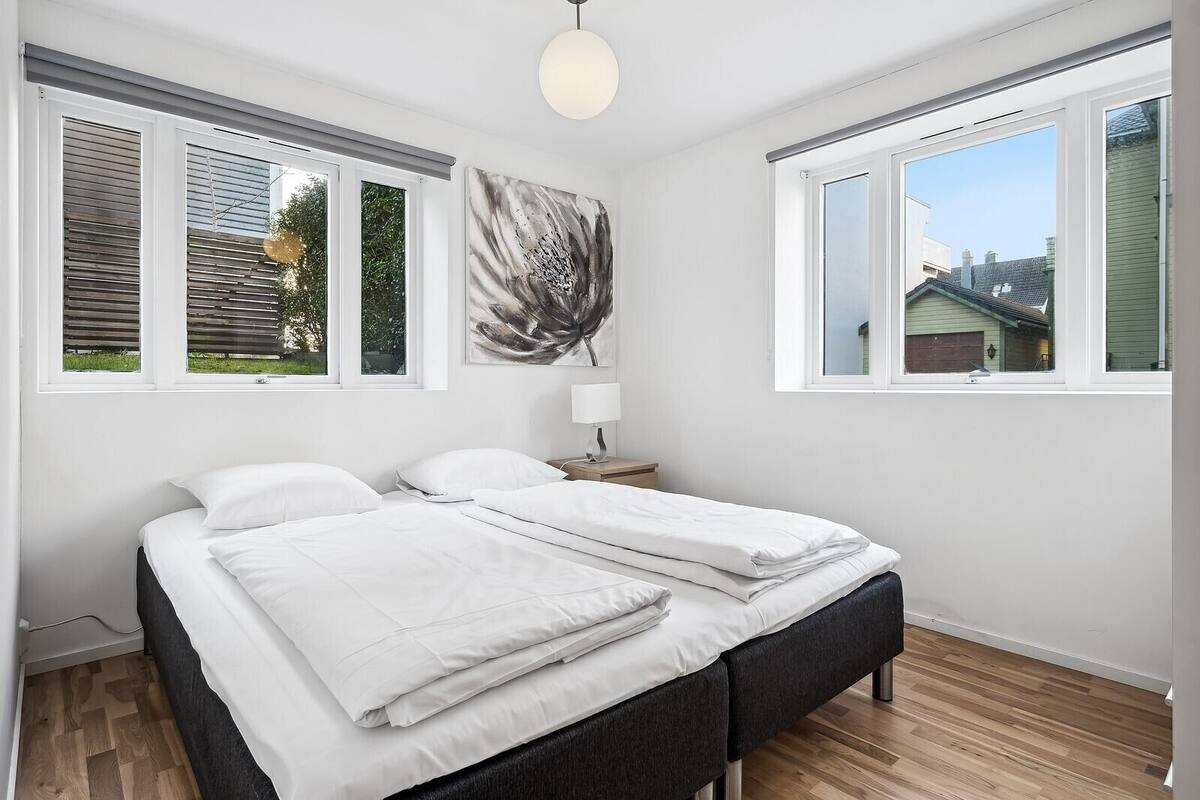 A bedroom with a bed, a nightstand, a lamp, and a window with a view of a house.
